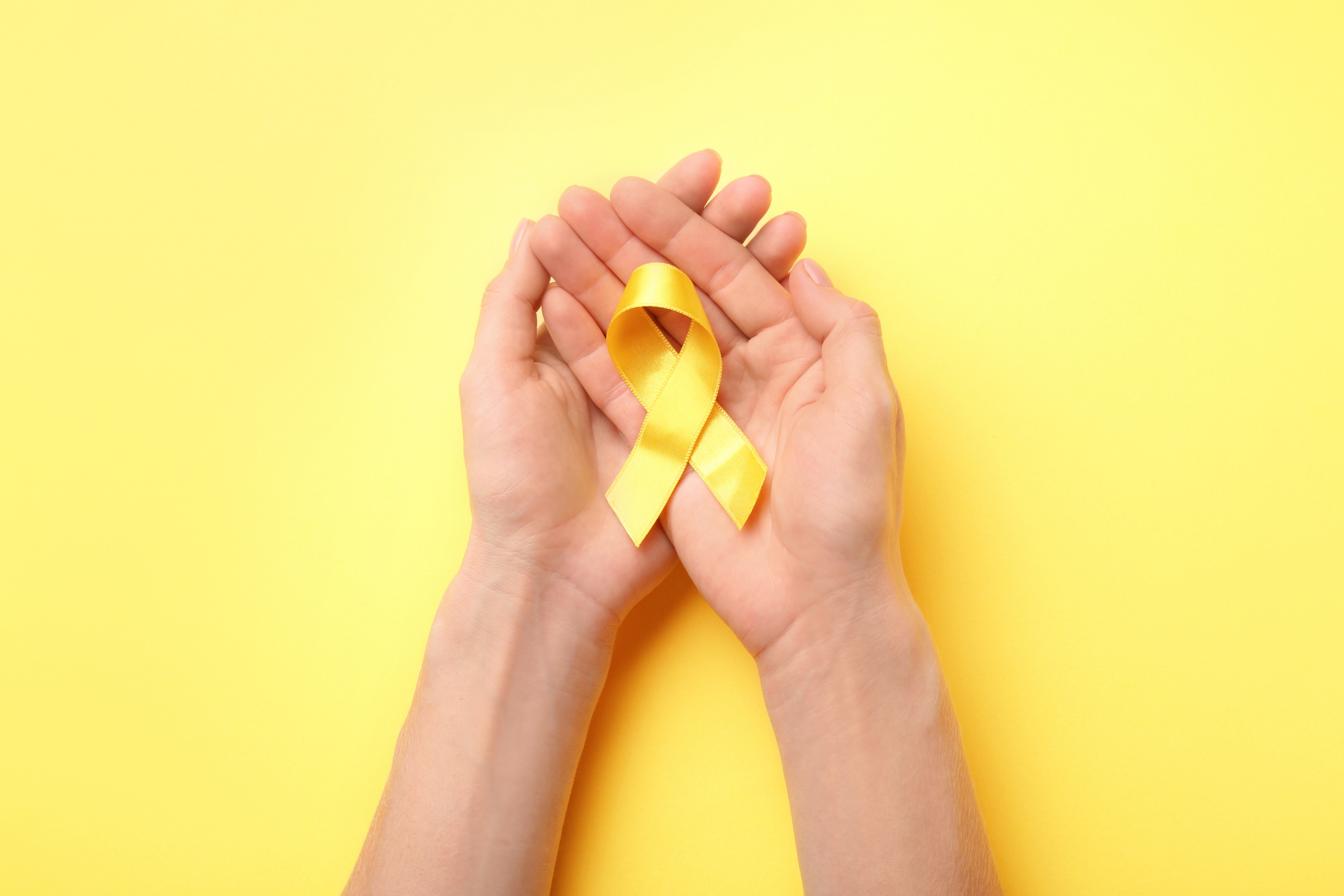 Female,Hands,Holding,Yellow,Ribbon,On,Color,Background.,Cancer,Concept